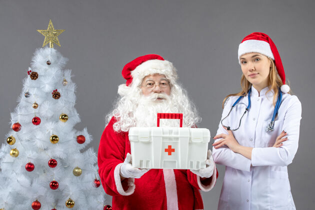 圣诞圣诞老人和给他急救箱的女医生在灰色墙上的正视图快乐节日圣诞老人