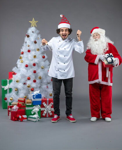 圣诞老人圣诞老人和男厨师在灰色墙上围着圣诞礼物的正视图前面礼物人