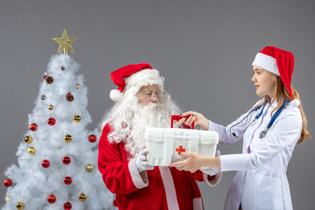 援助圣诞老人和给他急救箱的女医生在灰色墙上的正视图圣诞老人男性第一