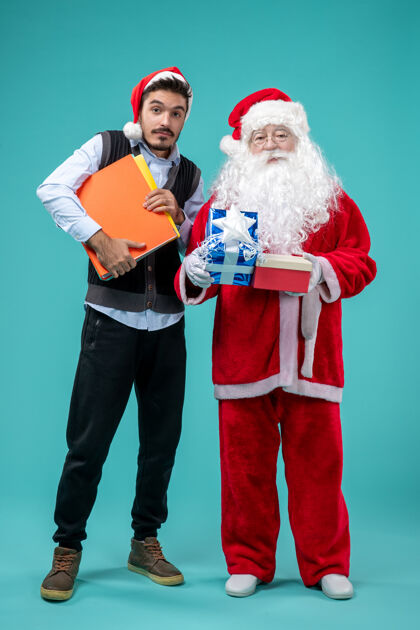 微笑前视图圣诞老人与年轻的男性和礼物上的蓝色背景男性圣诞前面