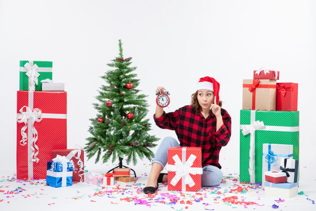 十二月前视图年轻女子坐在圣诞礼物周围拿着白色墙上的时钟庆祝礼物圣诞节