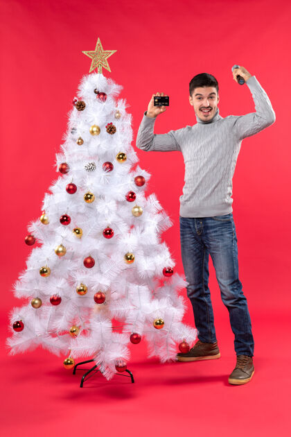 圣诞圣诞气氛 微笑的年轻人站在装饰好的圣诞树旁 手持麦克风和电话 展示他的力量家伙电话权力