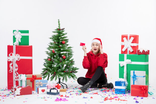 庆祝正面图：年轻女子围坐在白墙上 手里拿着红色的银行卡十二月圣诞前面
