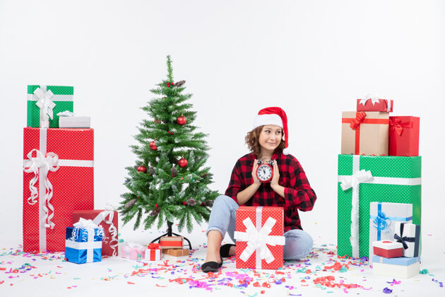 快乐前视图年轻女子坐在圣诞礼物周围拿着白色墙上的时钟坐人时钟
