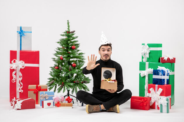 圣诞树正面图：年轻人围坐在白色的墙上 手里拿着圣诞礼物人礼物十二月