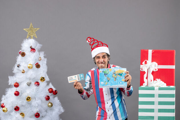 旅行者正面图笑人拿着世界地图和旅行票靠近白色圣诞树圣诞圣诞树礼物
