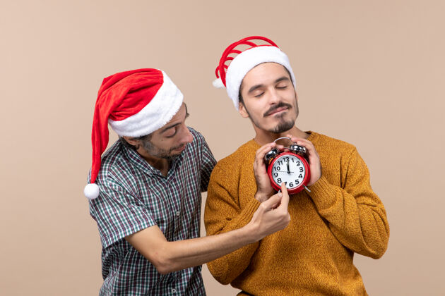 肖像前视图两个圣诞节男人一个拿着闹钟闭着眼睛 另一个显示在米色孤立的背景时间米色视图前面