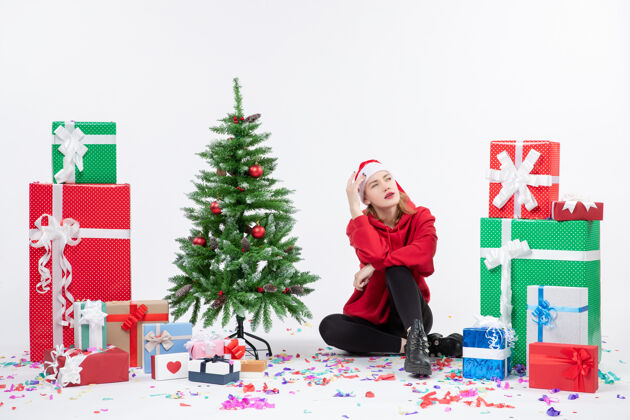 坐着年轻女子围坐在白色墙壁上不同节日礼物的前视图快乐圣诞快乐树