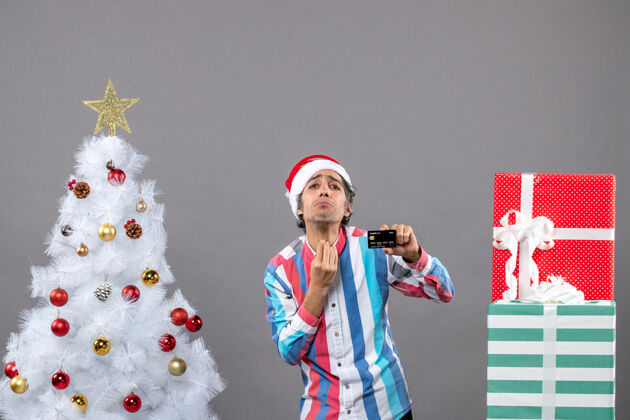 圣诞正面图：站在白色圣诞树旁展示亲吻标志的男子灰人吻