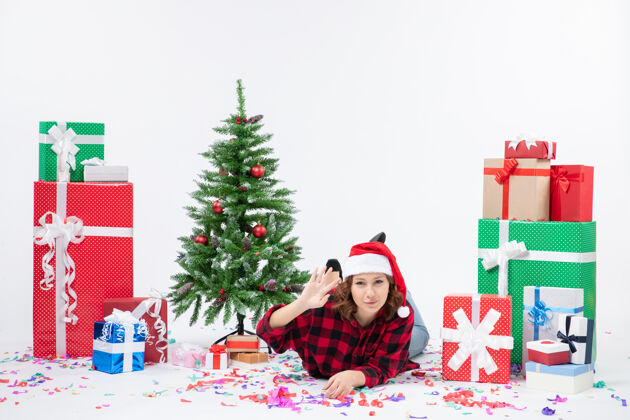 小正面图年轻女性躺在圣诞礼物和白色背景上的小圣诞树旁新年寒冷的女人圣诞节情感雪礼物寒冷铺设
