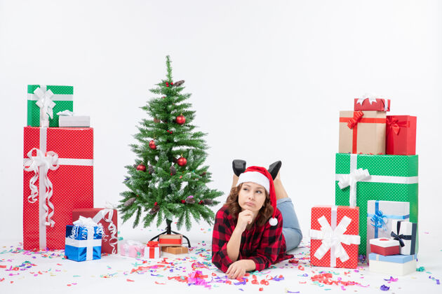 礼物前视图年轻女性躺在圣诞礼物和白色背景上的小圣诞树周围新年寒冷的女人圣诞雪圣诞寒冷铺设