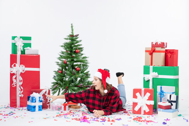 礼物正面图：年轻女性躺在圣诞礼物和小圣诞树周围 背景为白色 寒冷的女人 圣诞节 新年 下雪雪女性小