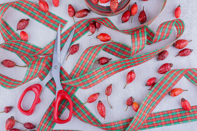 节日剪刀 圣诞糖果色的丝带和白色背景上的狗玫瑰果水果丝带装饰