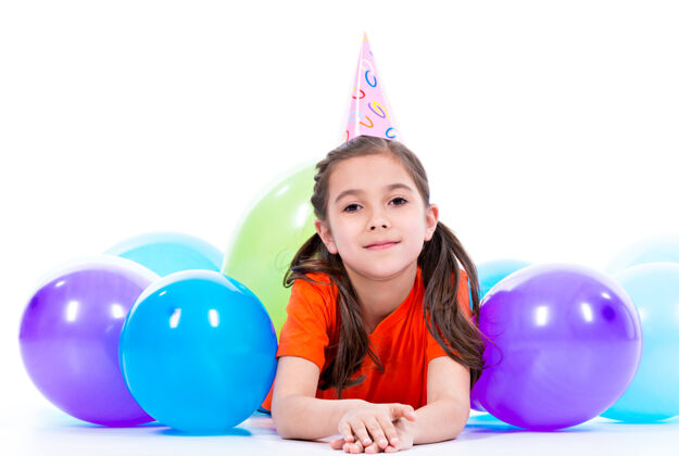 躺着穿着橙色t恤的快乐微笑女孩躺在地板上 带着五颜六色的气球-孤立在白色的地板上休闲孩子五颜六色