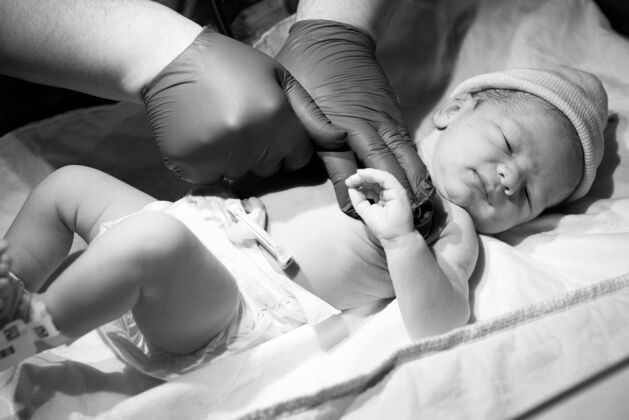 乳胶医生在医院灯光下检查新生儿的灰阶特写镜头床单色看