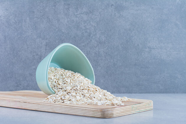 托盘燕麦片从大理石背景的小碗里倒在木板上营养燕麦片碗