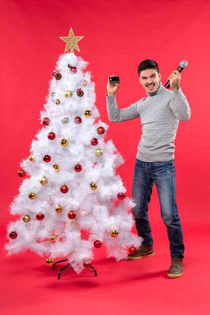 拿着圣诞气氛 年轻人站在装饰好的圣诞树旁 拿着麦克风拍照 为自己感到骄傲快乐雪人装饰