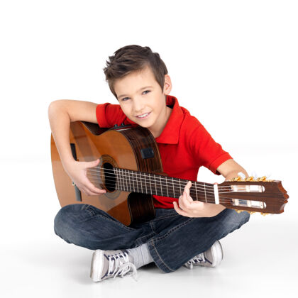 坐帅气的快乐男孩正在弹原声吉他-孤立演奏声学吉他手