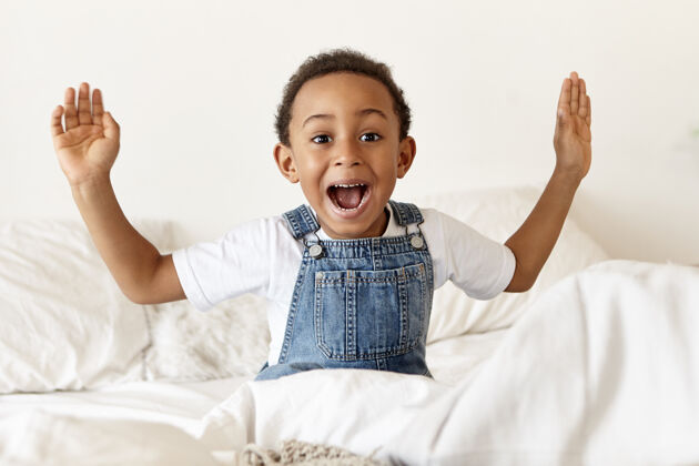自由情绪可爱的非洲裔小男孩坐在白色的床上兴奋床好玩