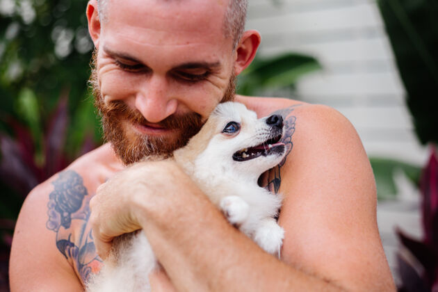 伴侣年轻英俊的胡须野蛮的纹身快乐男人抱着波美拉尼亚斯皮茨玩可爱的宠物快乐人纯种