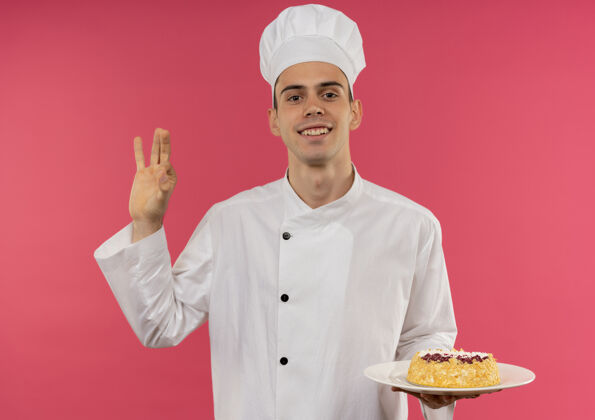 手势年轻的男厨师面带微笑 身穿厨师制服 手拿蛋糕放在盘子里 摆出很好的姿势厨师盘子厨师