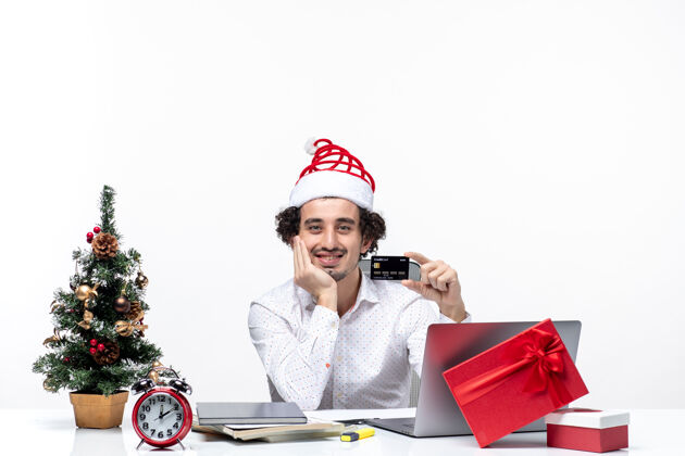 举行带着微笑的商务人士 戴着圣诞老人的帽子 手里拿着银行卡 手放在办公室的下巴下面 节日的喜庆气氛下巴商务成人