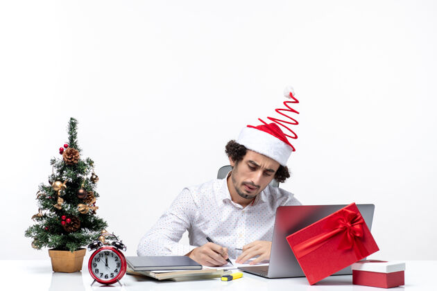 成年人专注的年轻商人 戴着有趣的圣诞老人帽子 在白色背景的办公室里检查庆祝圣诞节的便条写作集中圣诞节