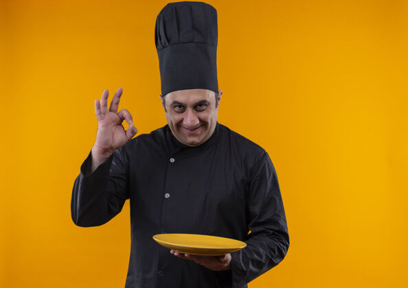 好的微笑的中年男厨师身着厨师制服 在黄色背景上展示okey手势托板 并留有复印空间厨师拿着厨师