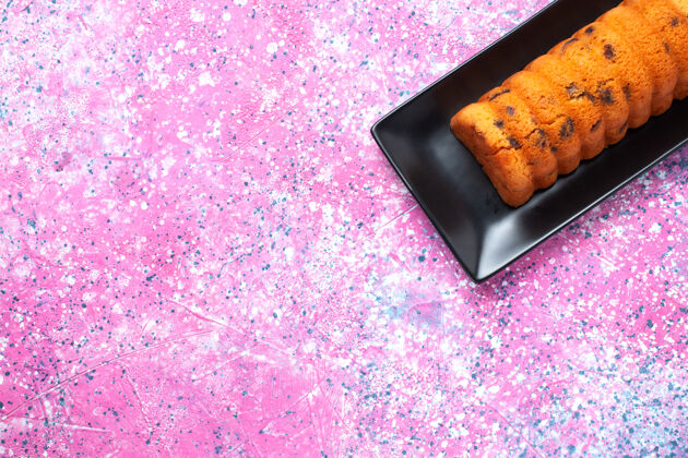 棕色在粉红色桌子上的黑色蛋糕锅里俯瞰美味的烤蛋糕茶盘子饼干