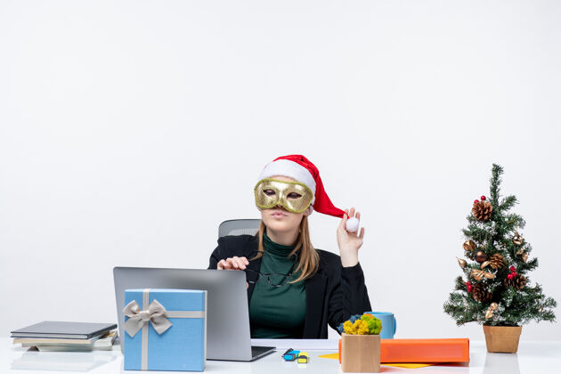 女人圣诞节心情与年轻女子玩圣诞老人哈塔戴着面具坐在一张桌子上的白色背景镜头笔记本电脑镜头桌子