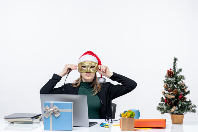 帽子圣诞节心情与年轻女子戴着圣诞老人的帽子 戴着面具坐在一张白色背景的股票照片表办公室圣诞老人面具