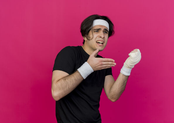 手指年轻的运动型男子穿着运动服 戴着头巾 胳膊指着缠着绷带的手腕 感到疼痛戴运动装年轻
