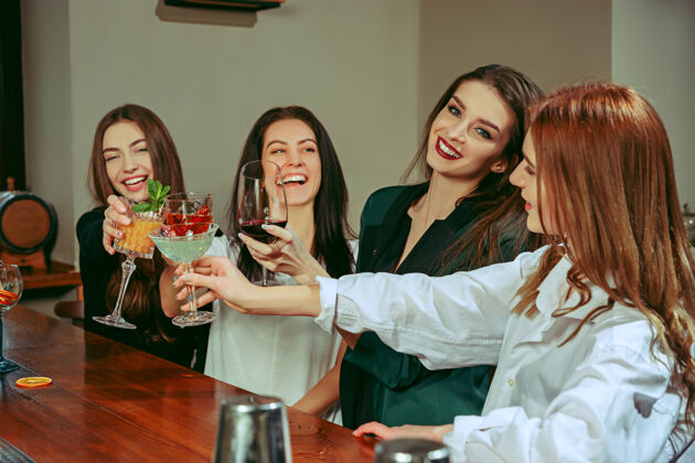手女朋友在酒吧喝酒她们坐在一张有鸡尾酒的木桌旁水果俱乐部友谊