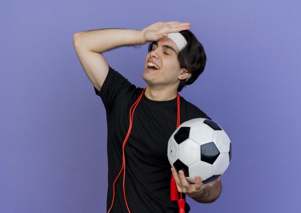 手年轻的运动型男子 穿着运动服 戴着头巾 脖子上系着跳绳 手里拿着足球 一副迷茫的样子 手放在头上 犯了错误头带运动装脖子