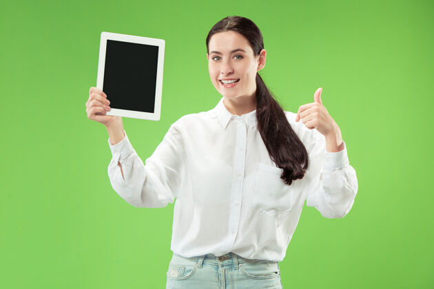 成人一个自信的休闲女孩的肖像 显示绿色背景下笔记本电脑的空白屏幕惊讶手机惊讶