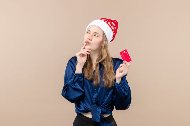 银行正面图年轻女性手持红色银行卡 背景为粉色圣诞钱照片 节日新年感慨女性情感钱