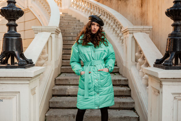 街头时尚女人摆出冬秋时尚潮流蓝色羽绒服和帽子贝雷帽在古老美丽的街道楼梯城市户外街头风格