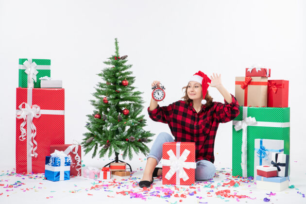 人前视图的年轻女子坐在圣诞礼物周围拿着白色墙上的时钟前面情感节日
