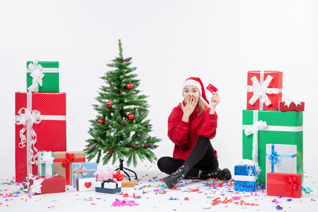 人正面图：年轻女子围坐在白墙上 手里拿着红色的银行卡礼物人圣诞树