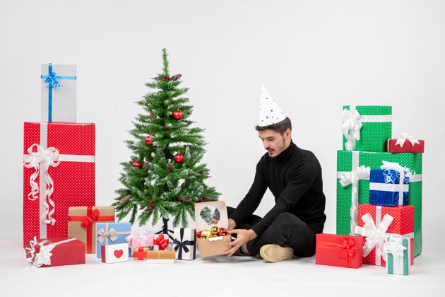 圣诞树正面图：年轻人围坐在节日礼物旁边 拿着一个白色墙上的玩具包十二月节日情感
