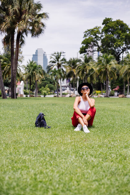 公园快乐女人背着背包环游曼谷 在绿草如茵的热带公园里享受美丽的晴天草地美丽休息
