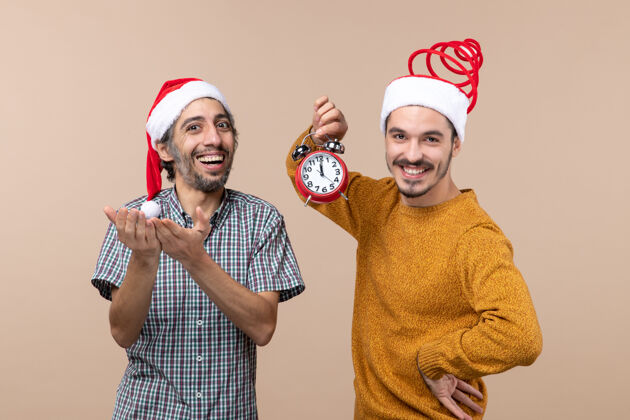 微笑正面图两个快乐的男人拿着闹钟 在米色孤立的背景上微笑男人视图肖像