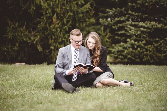 公园一对浪漫的情侣坐在草地上 深情地读着一本书草坪女人夫妇