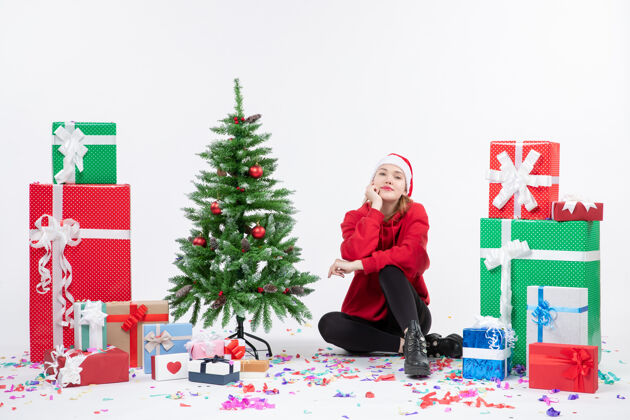 十二月年轻女子坐在白色墙壁上围着节日礼物的正视图人礼物人