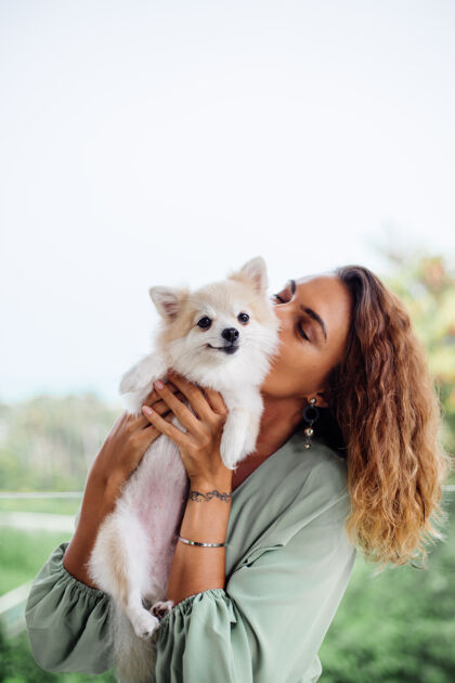 关怀欧洲棕褐色卷曲女人的户外肖像抱着快乐的宠物狗波美拉尼亚斯皮茨可爱幸福年轻
