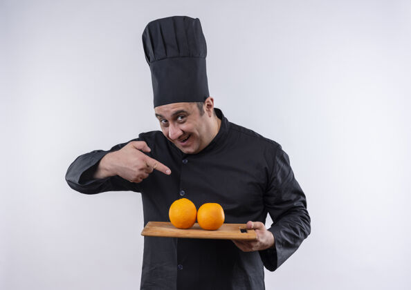 手身着厨师制服的快乐中年男厨师用手指着孤立的白墙上砧板上的橘子中年切割手指