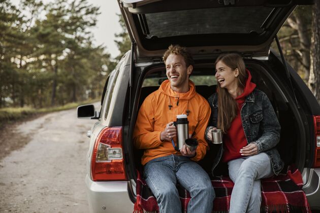 公路在汽车后备箱里享受热饮料的幸福夫妇的正面图公路旅行饮料户外