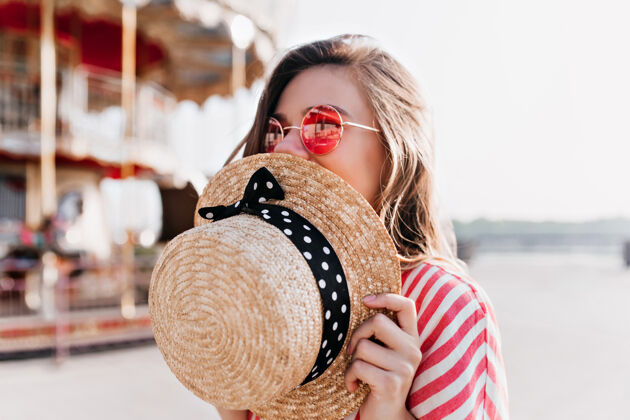 金发幸福的金发女孩戴着草帽 在夏日里摆姿势戴着粉色太阳镜的快乐年轻女子在游乐园休息的户外照片休息女性微笑