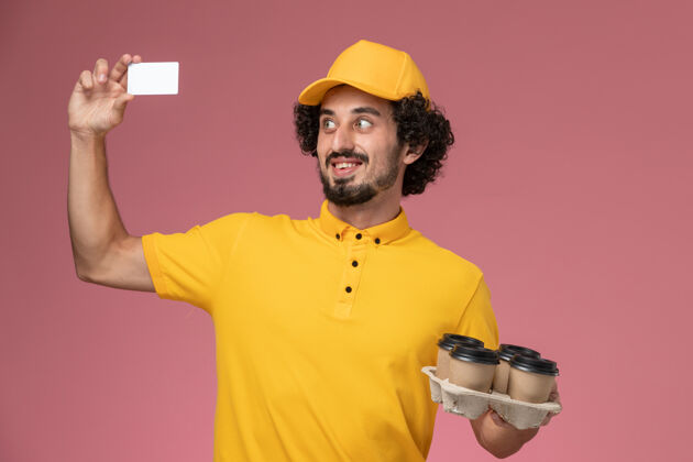 制服正面图：身穿黄色制服的男信使手拿棕色咖啡杯 粉色墙上挂着白色卡片男性棕色服务