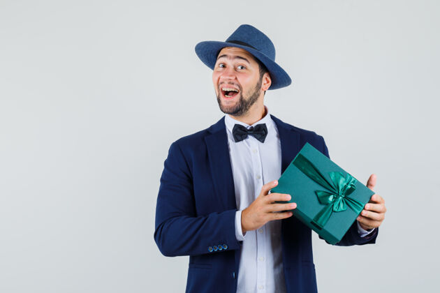 英俊年轻人穿着西装 戴着帽子 手里拿着礼物盒 看上去很高兴正面图生日礼物礼物
